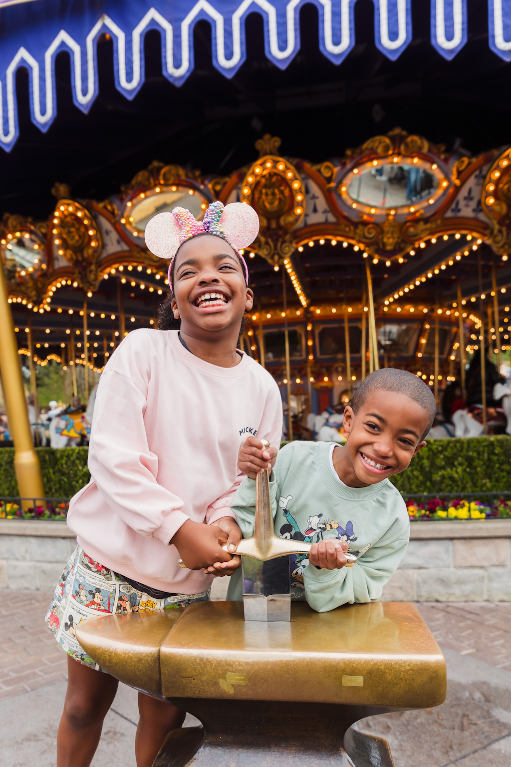 Two laughing children attempt to pull the sword from the stone in Disneyland on their Flytographer photoshoot.