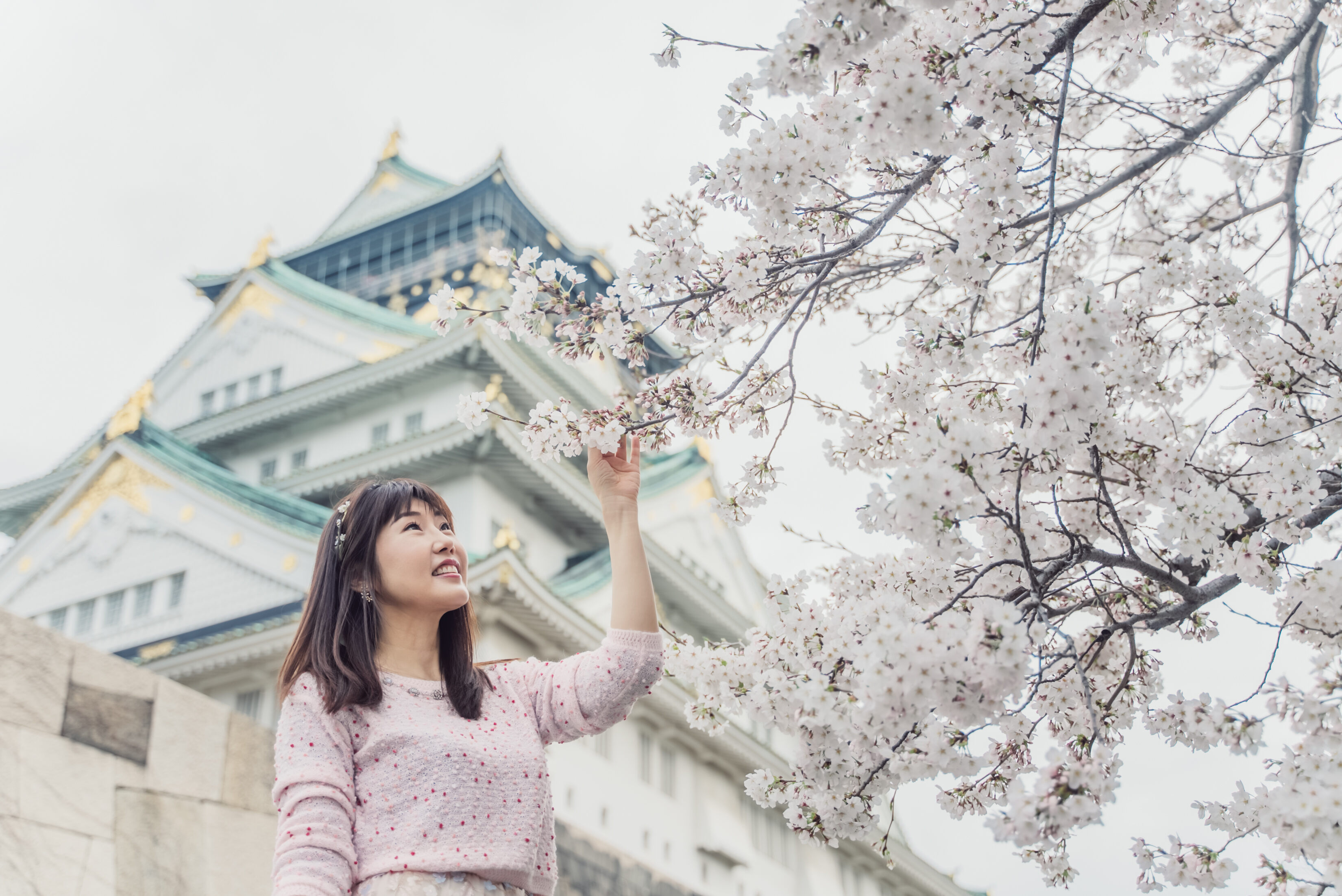 A girl posing in front of Osaka Castle during cherry blossom season