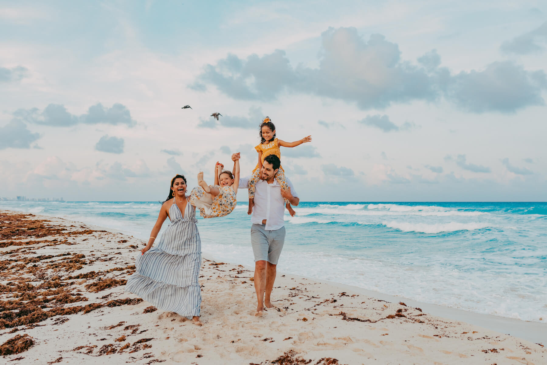 A family laughing and playing together on the beach in Cancun, Mexico on a family photoshoot with Flytographer.