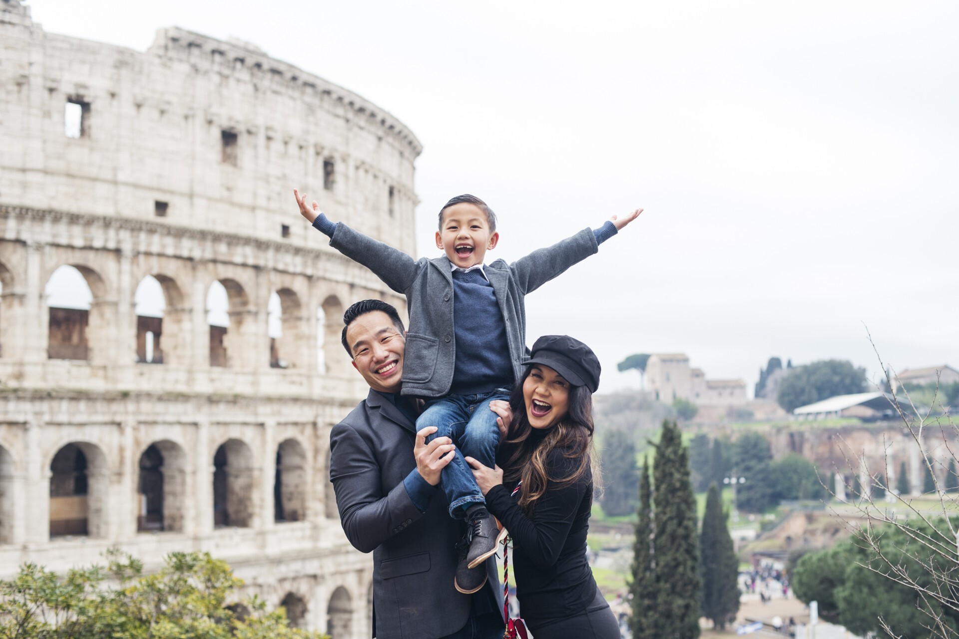 A smiling couple holds their son on their shoulders in Rome in front of the Colosseum during their Flytographer shoot
