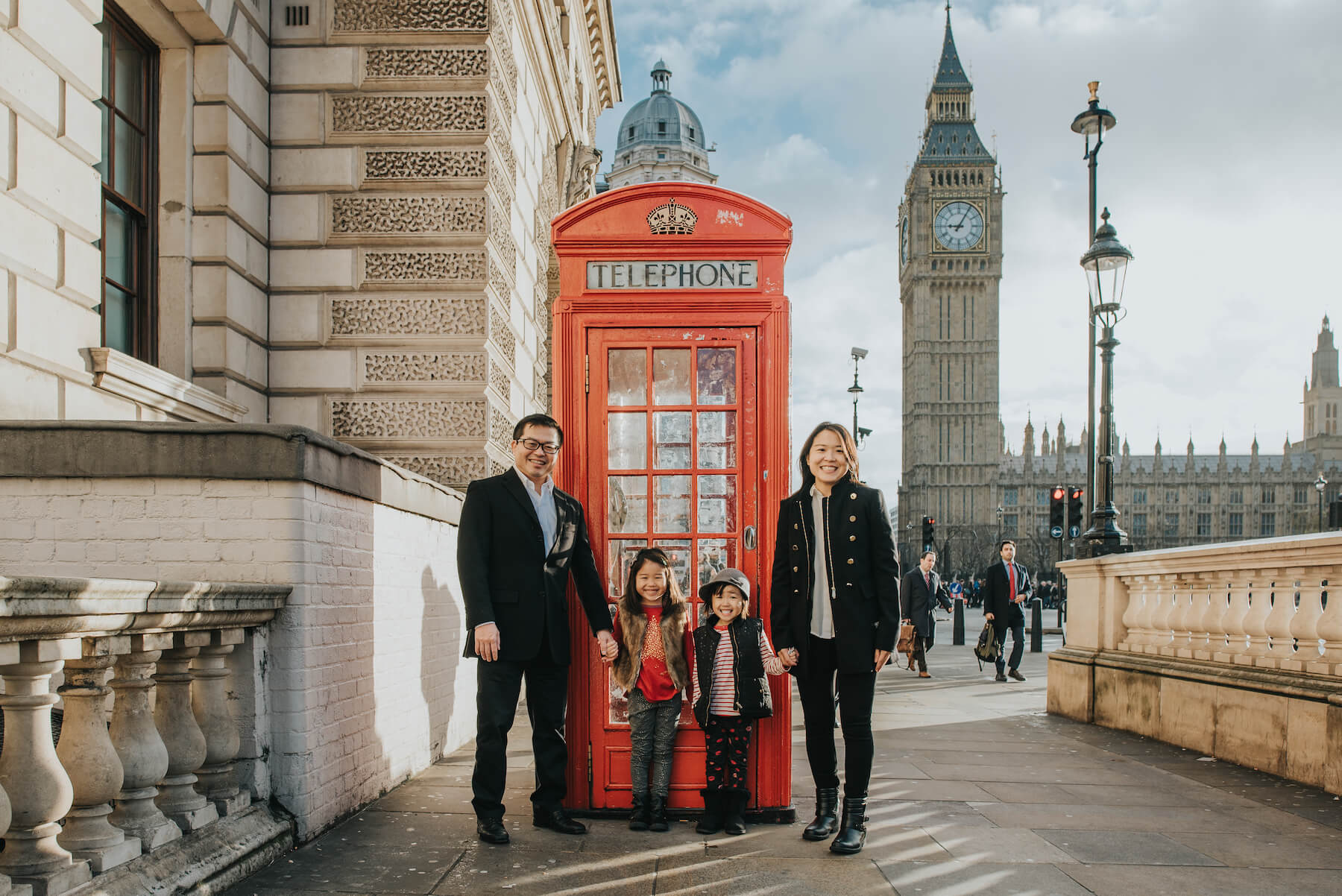 A family holding hands in front of the Big Ben and a red telephone booth on a family photoshoot in London with Flytographer