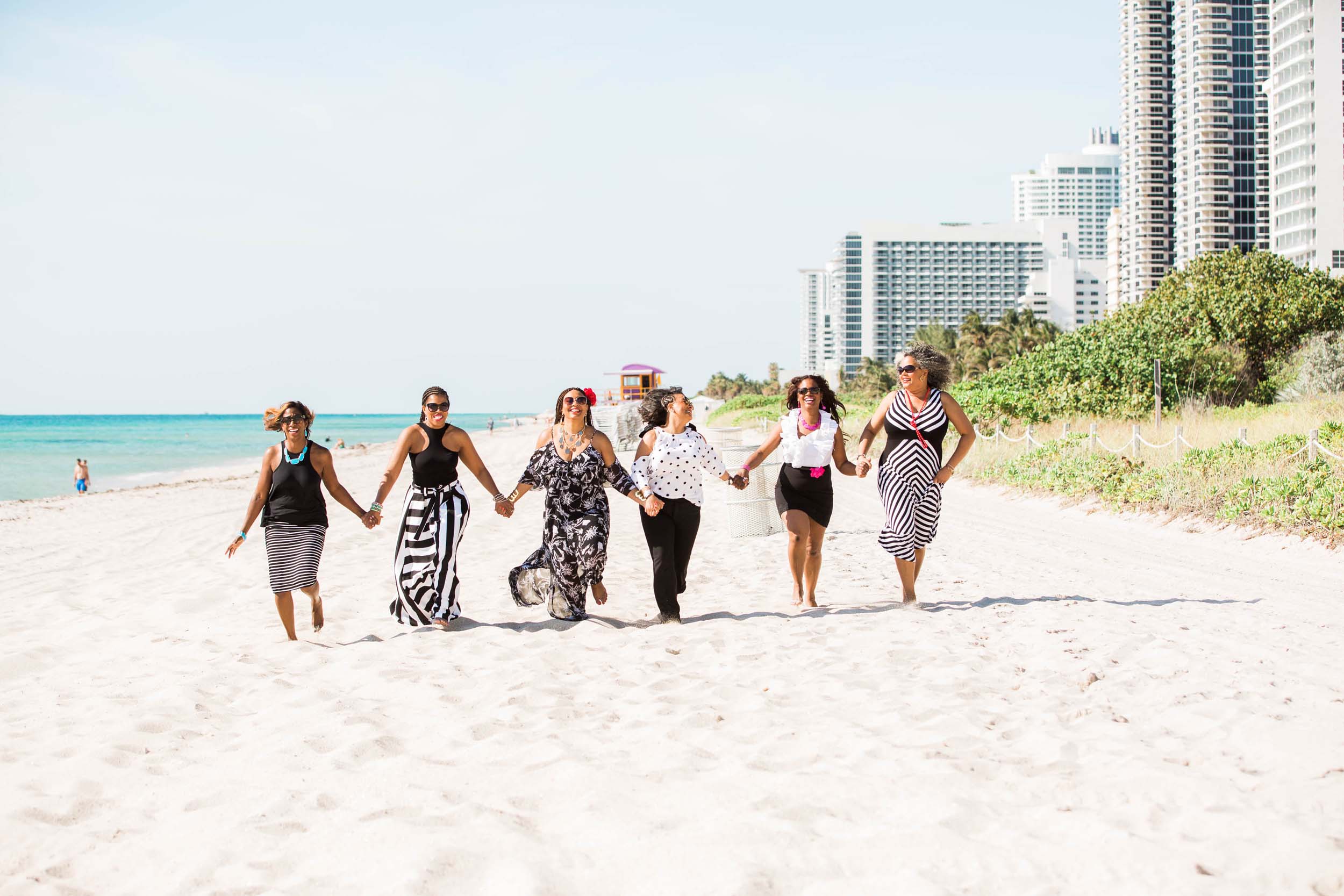 A group of women walking and holding hands on the beach in Miami on a photoshoot with Flytographer