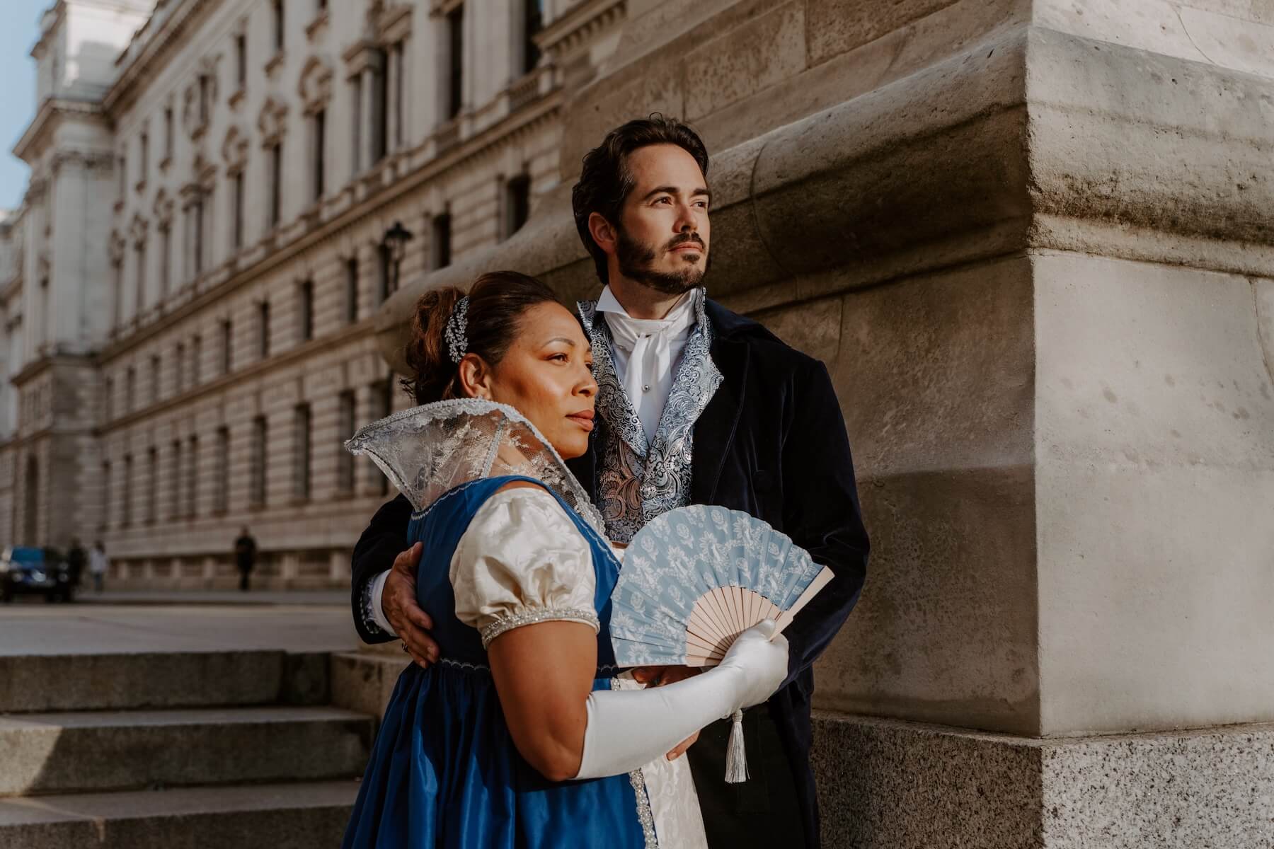 A couple looking into the distance dressed in Bridgerton-inspired outfits on a couple photoshoot in London with Flytographer.