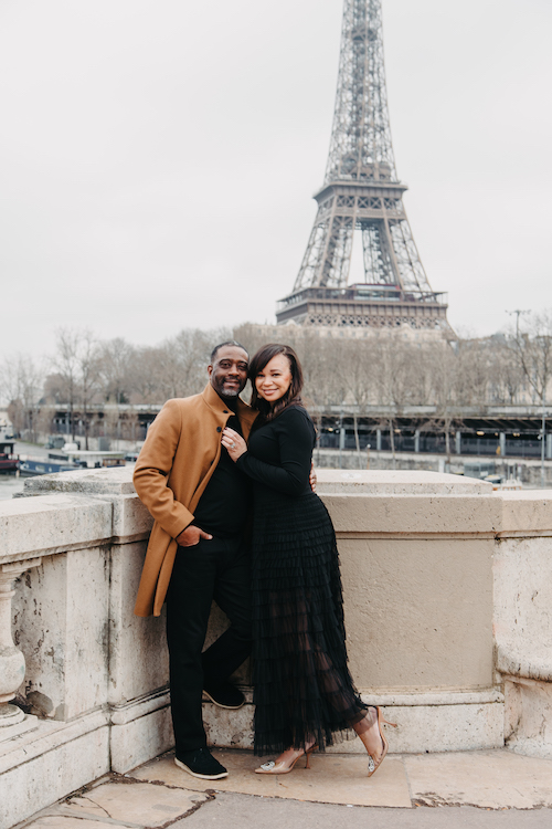 A smiling couple poses in front of the Eiffel Tower in Paris on their Flytographer photoshoot.