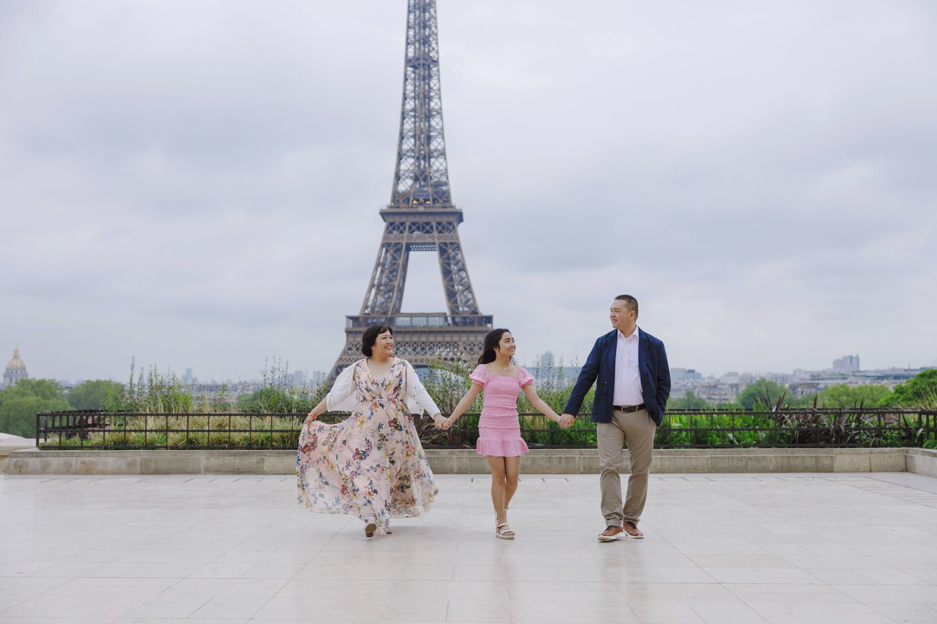A smiling family of three holds hands and walks in front of the Eiffel Tower on their Flytographer photo shoot