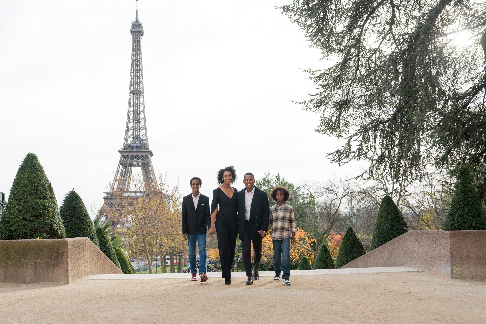 A smiling family of four holds hands and walks in front of the Eiffel Tower on their Flytographer photo shoot