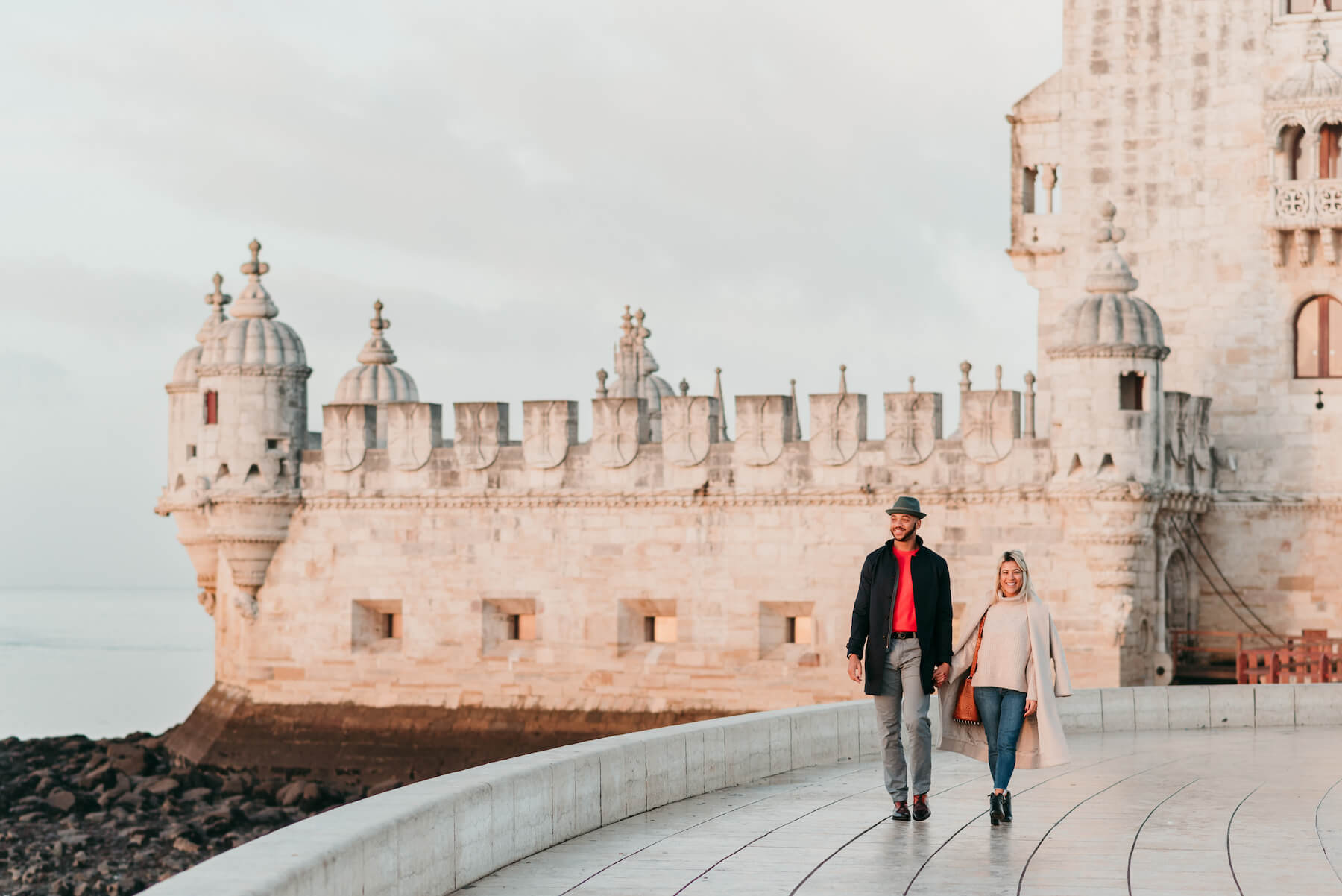 A couple walking at Belem Tower in Lisbon on an engagement photoshoot with Flytographer