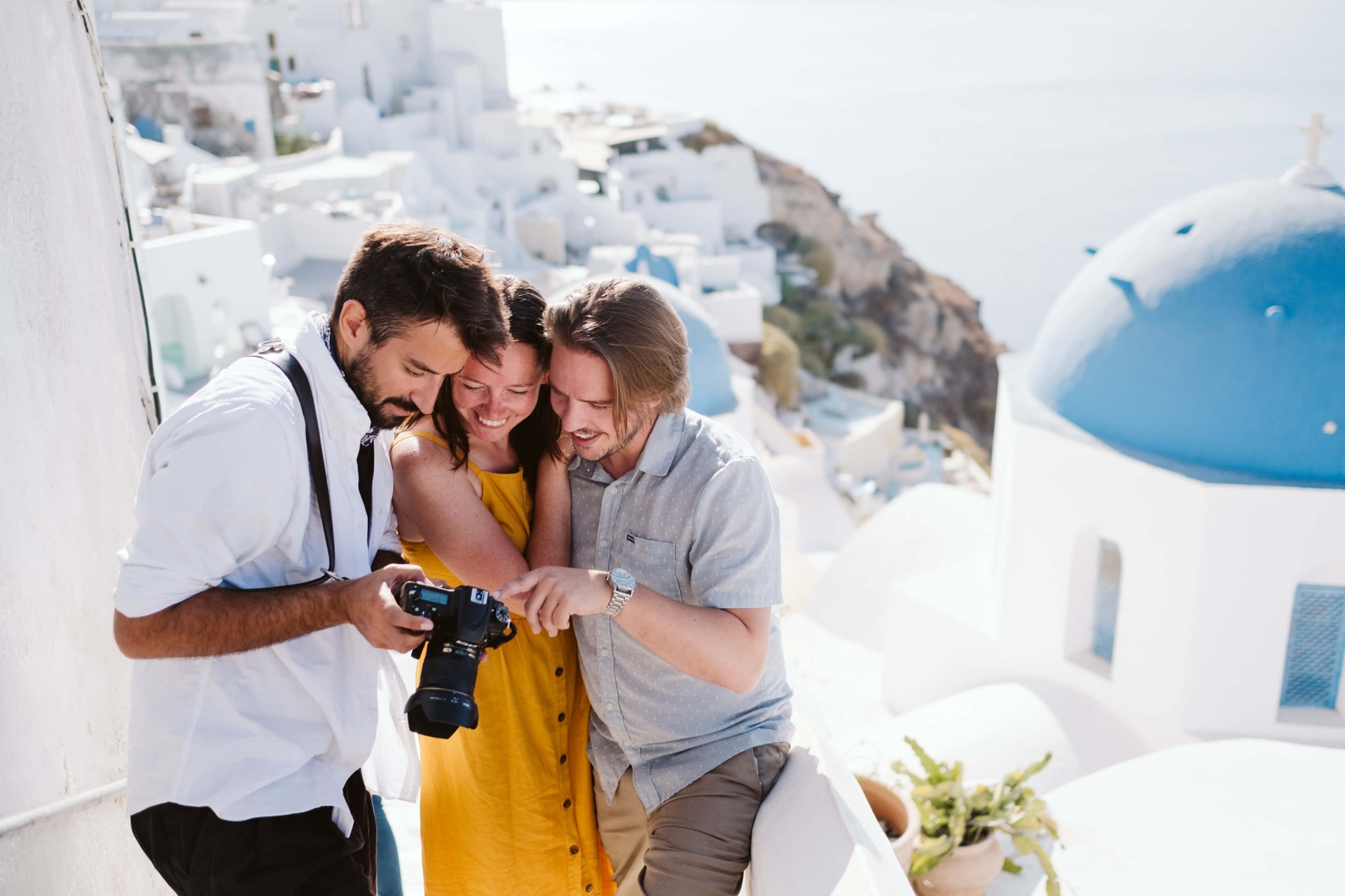 A smiling photographer shows a photo on his camera to a couple in Santorini during their Flytographer shoot