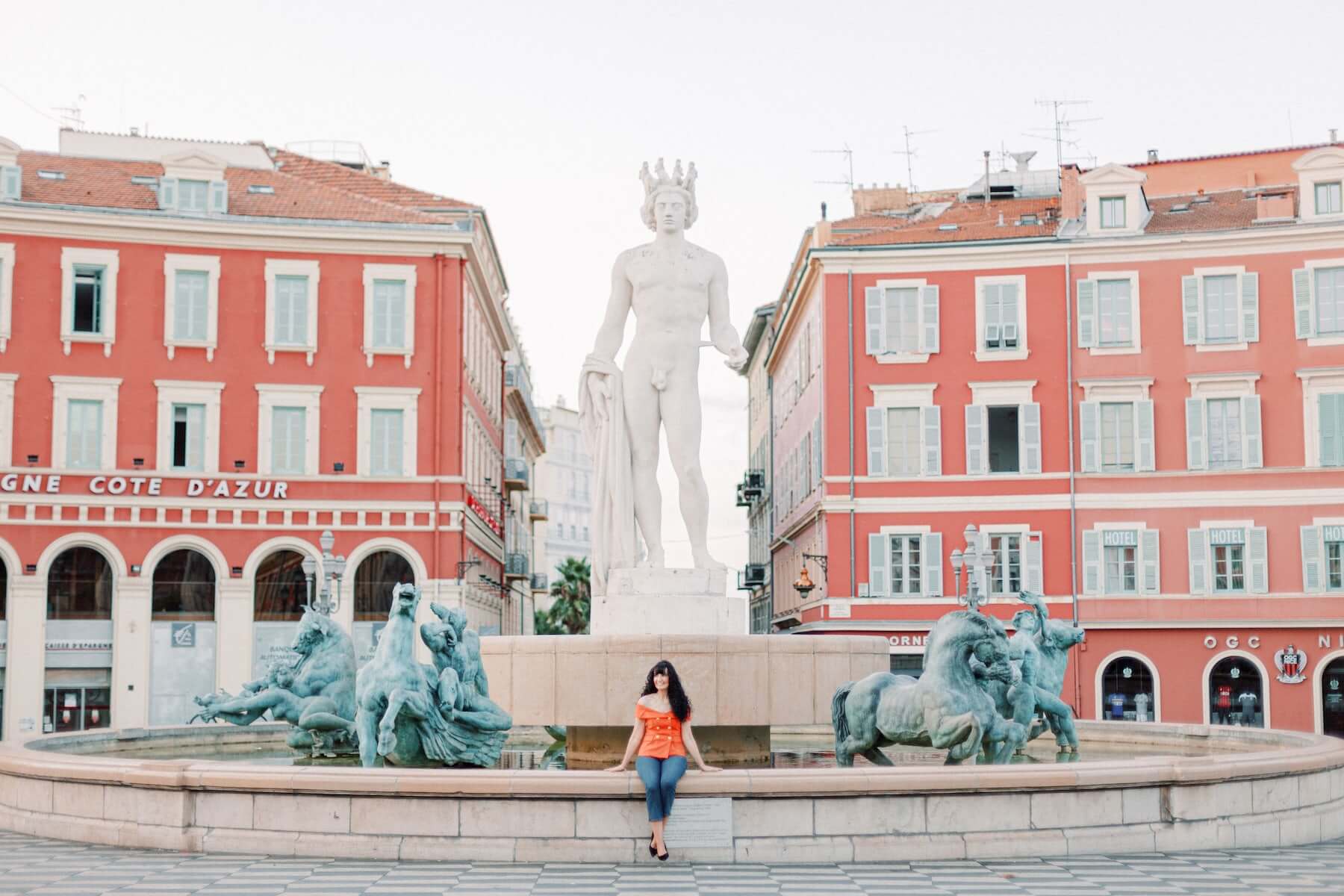 A woman sits in front of the Sun Fountain in Place Masséna in Nice, France