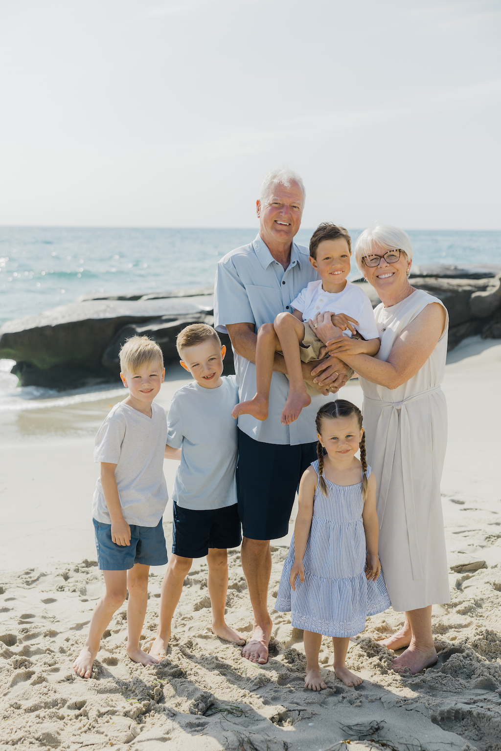 Smiling grandparents pose with their grandchildren on a beach in San Diego on their Flytographer photoshoot.